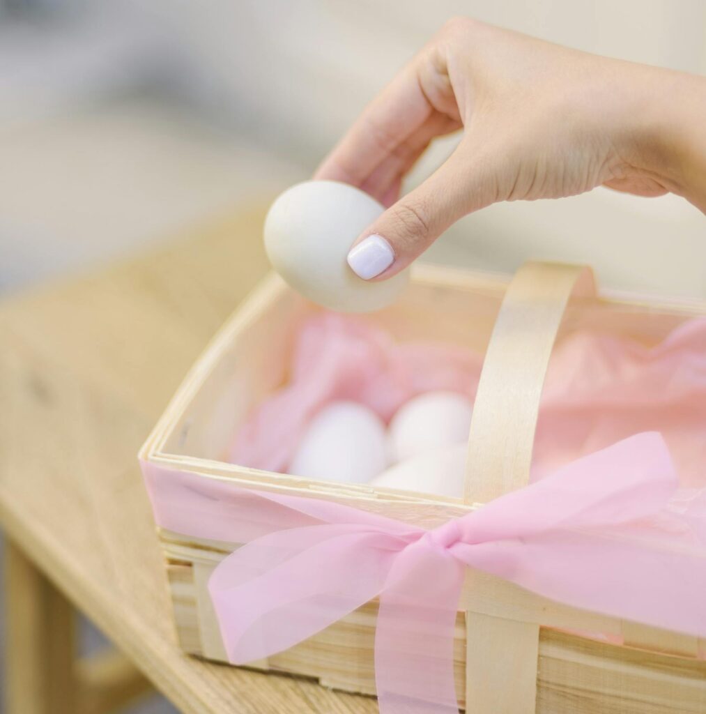 Hand gently placing an Easter egg in a ribbon-decorated basket, perfect for spring celebrations.