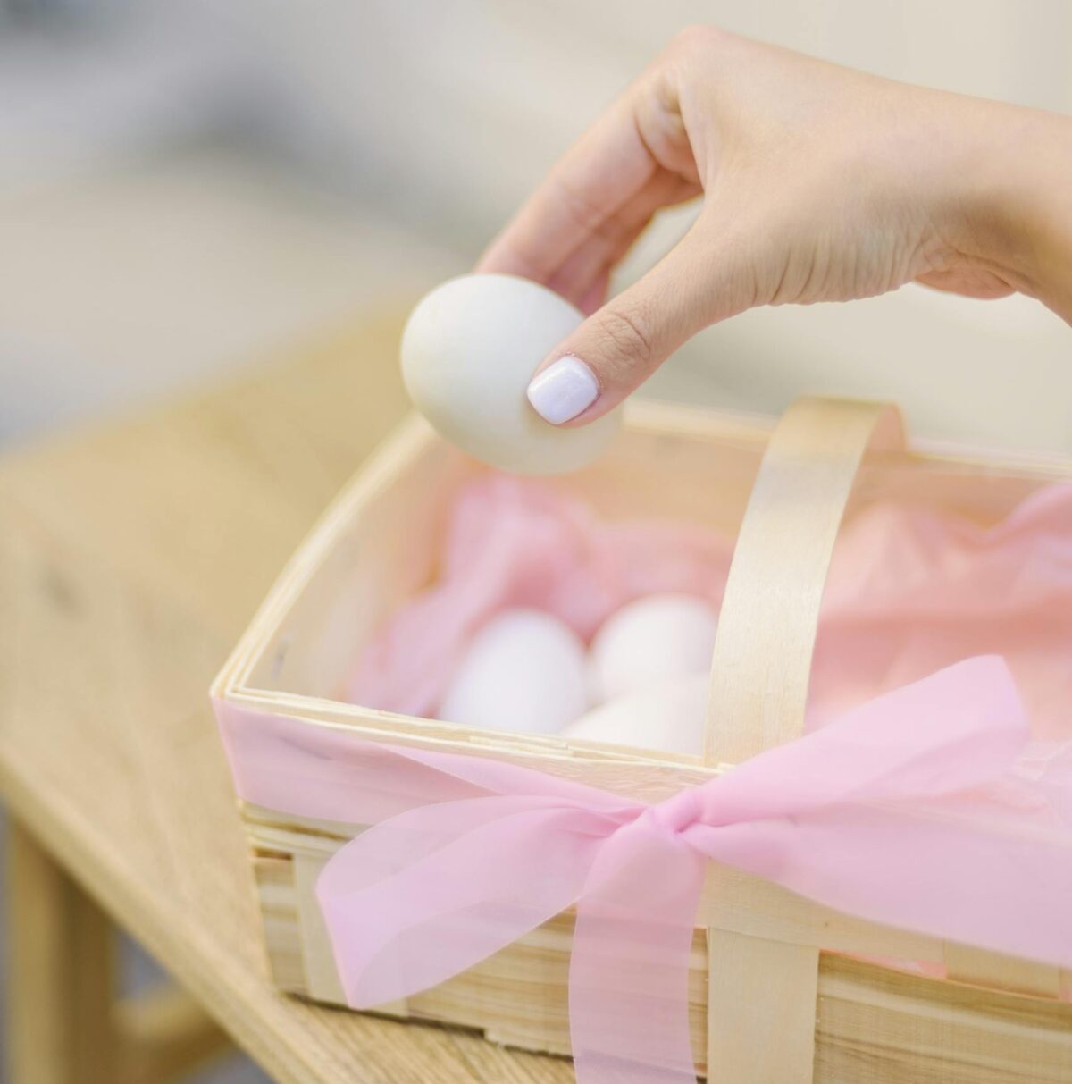 Hand gently placing an Easter egg in a ribbon-decorated basket, perfect for spring celebrations.